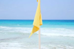 Yellow flag on Cancun beach indicating caution advised due to moderate currents or waves, suggesting swimmers should be careful.