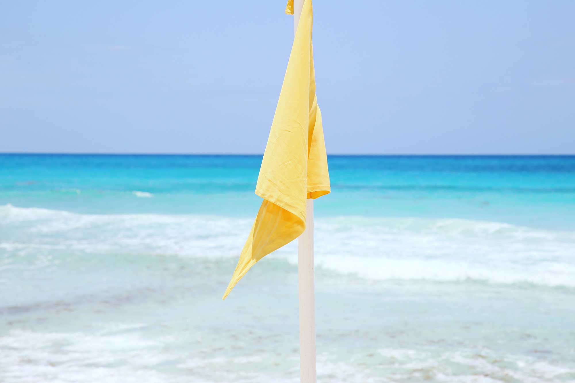 Yellow flag on the beach in Cancun advises swimmers to exercise caution due to moderate waves and currents. Yellow flag on Cancun beach indicating caution advised due to moderate currents or waves, suggesting swimmers should be careful.