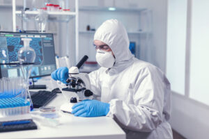 Doctor looking at sample of coronavirus using microscope in modern laboratory. Virolog in coverall during coronavirus outbreak conducting healthcare scientific analysis.