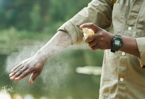 Person applying mosquito repellent in a tropical setting in Cancun, demonstrating dengue prevention with lush greenery and beach background