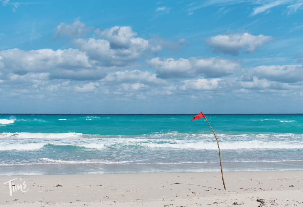 Red beach safety flag flying in front of Tim’s Ocean Condos in Cancun, warning of strong waves and no swimming conditions.