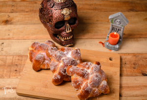 Pan de Muerto on a wooden board with a decorative skull and RIP candle for Day of the Dead