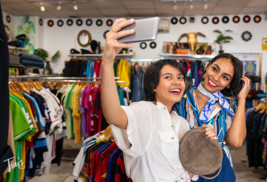 Two women browsing items together while shopping, enjoying the experience and looking at various products in a lively market setting.