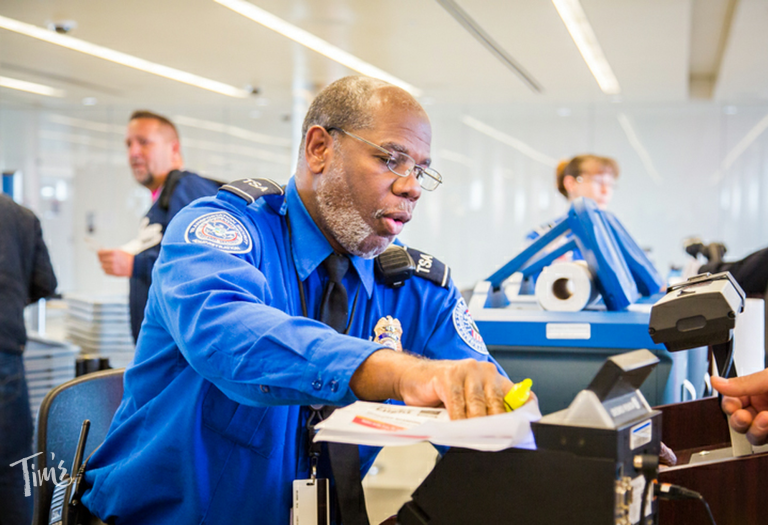 A TSA agent carefully inspects a passenger’s REAL ID at an airport security checkpoint in 2025.