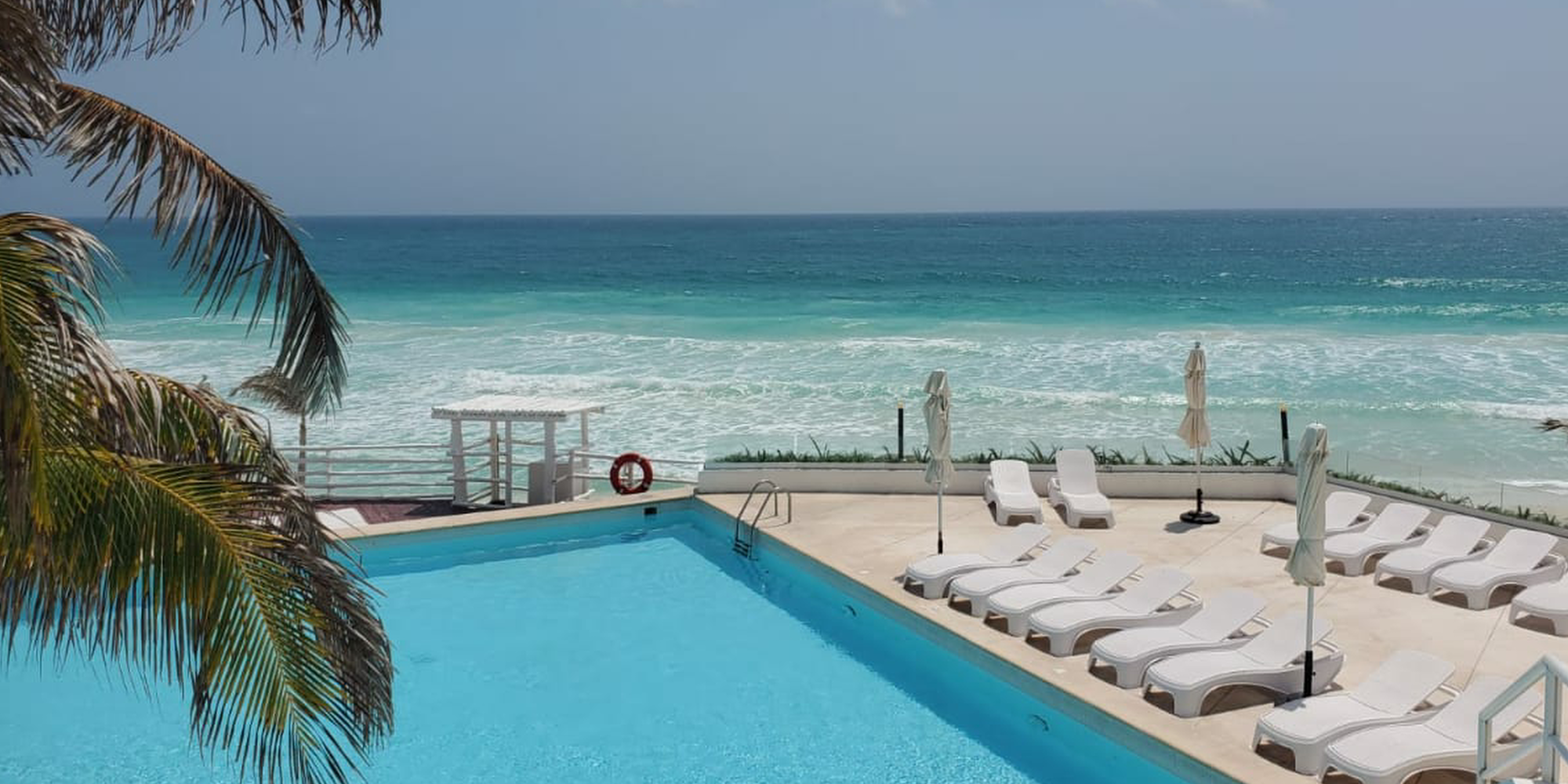 Beachfront vacation rental pool at Tim’s Ocean Condos in Cancun with ocean views and white lounge chairs.