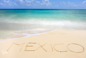 The word Mexico written in the sand on our Cancun beach with turquoise Caribbean waters in the background.