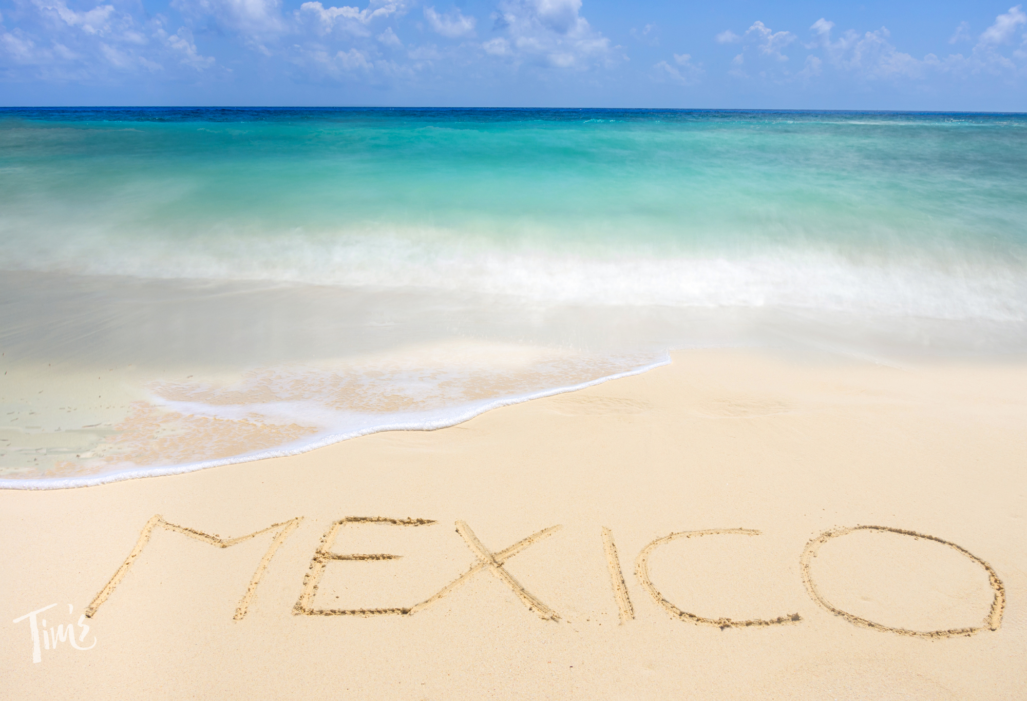 The word Mexico written in the sand on our Cancun beach with turquoise Caribbean waters in the background.